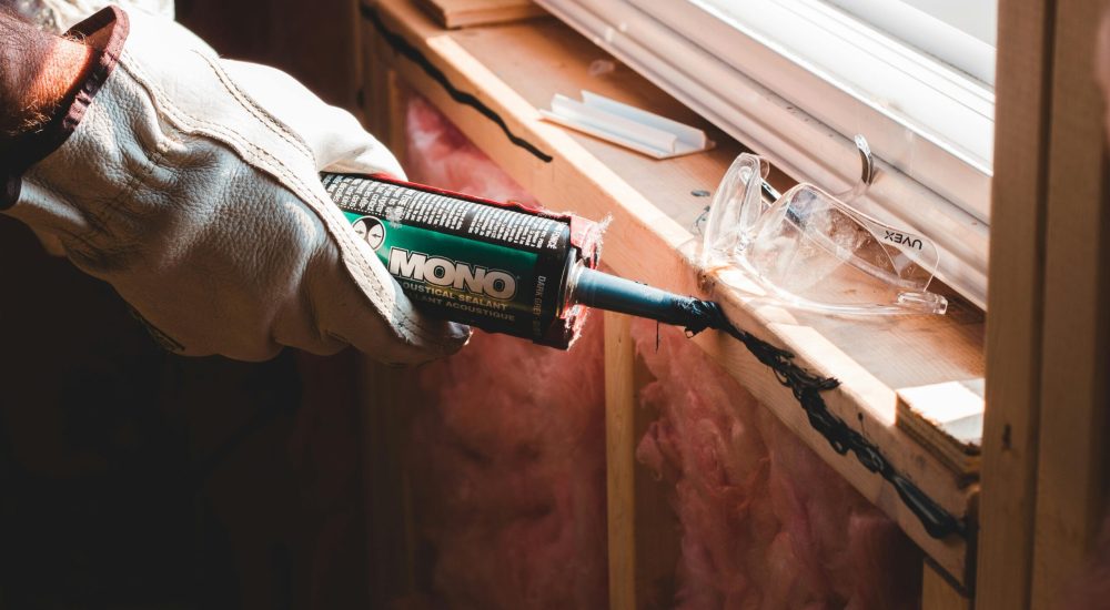 Crop unrecognizable workman in glove applying caulk from bottle on seam during window montage work in building